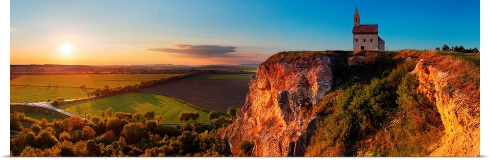 Panoramic image of a church on a cliff overlooking a village in Slovakia at sunset.