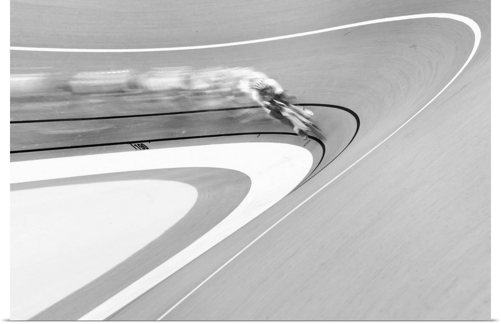 Black and white image of a cyclist in a velodrome coming around a curve.