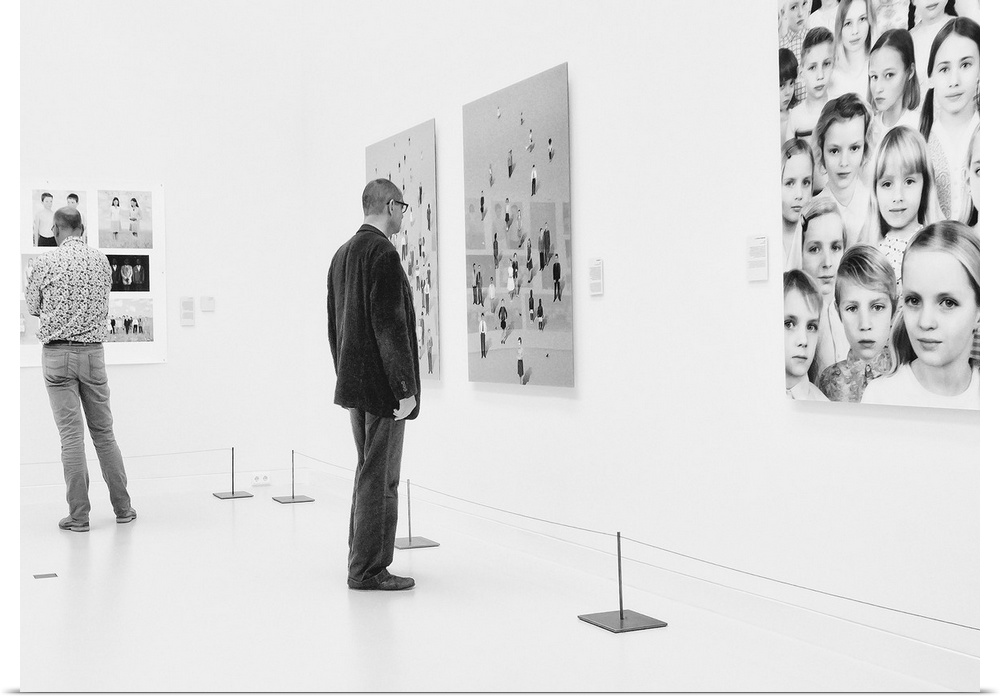 A man in an art gallery looks at figurative artwork on the wall.