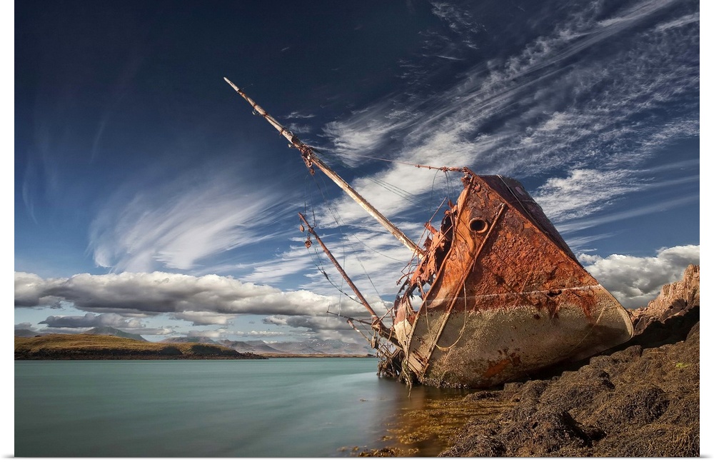 A abandoned ship sits on the shoreline, covered in rust, Stykkisholmur, Iceland.