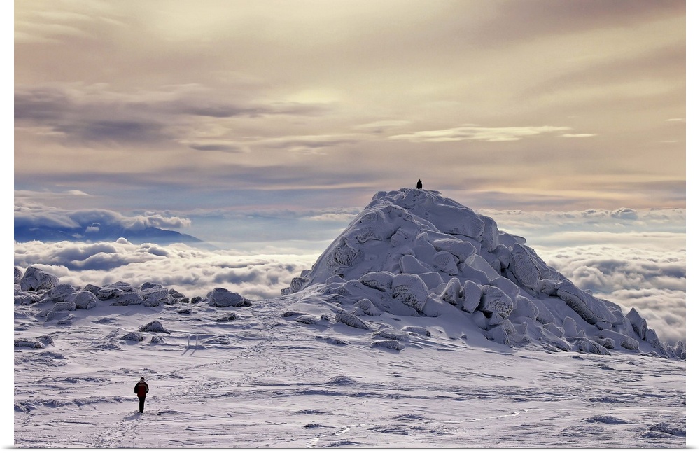 A figure walks across a snowscape on a mountain top, with another figure on a hill in the distance, a sea of clouds below.