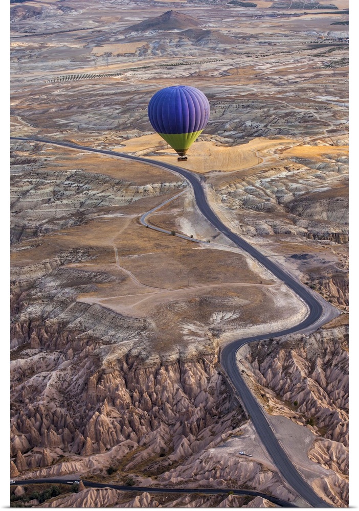 A blue hot air balloon flying high above a rugged and arid looking landscape.