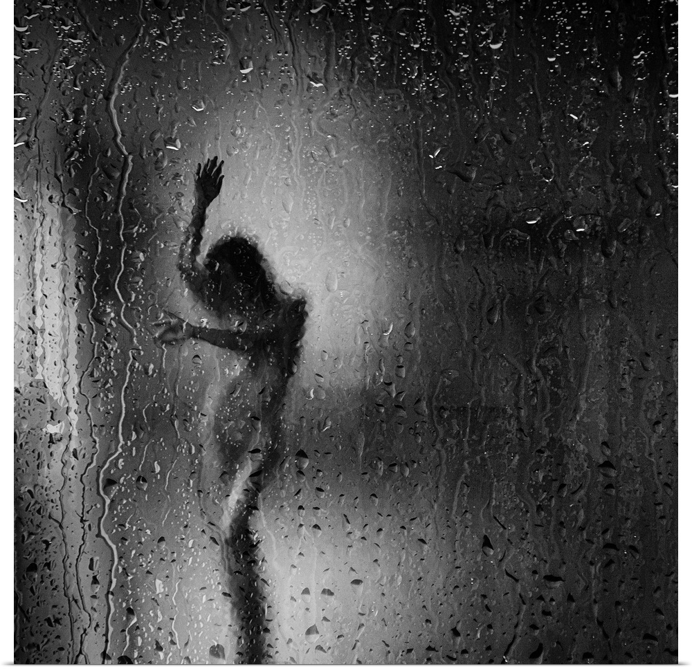 Square black and white fine art photograph of a nude woman through a rainy window glass.