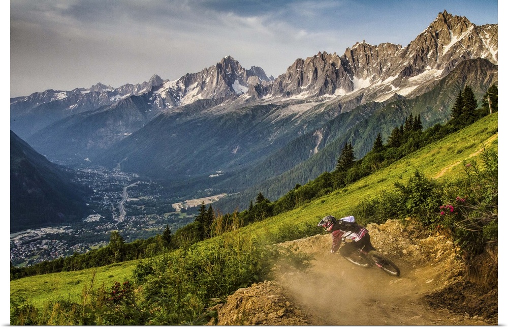 A mountain biker kicking up dust from while riding a trail, with a spectacular mountain range in the background.