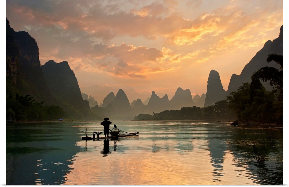 A fisherman and his cormorants on a boat in the Li River at dawn, China.