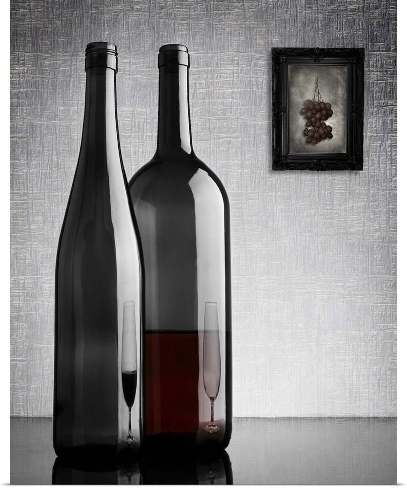 Two glass wine bottles with reflections of glasses on them, and a framed image of grapes on the wall.
