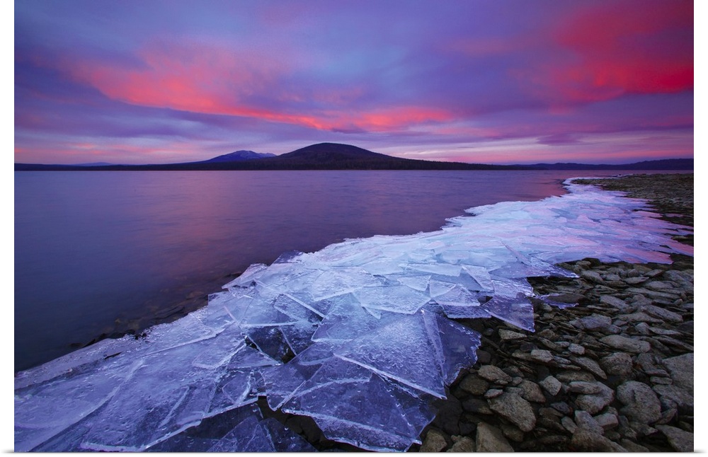 Cracked ice sheets on a rocky shore at sunrise.
