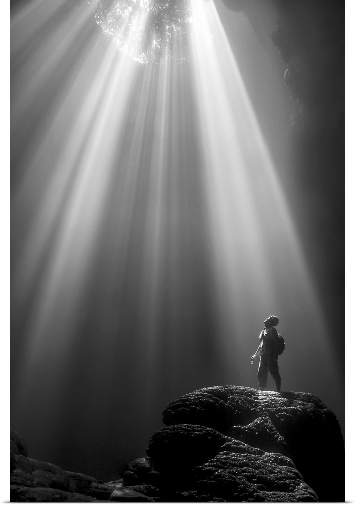 A person standing on a rock under beams of light shining into Jomblang Cave, Indonesia.