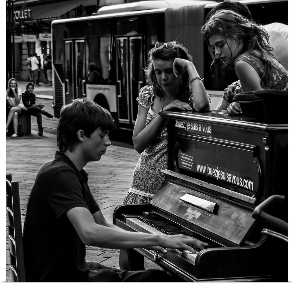 A black and white photograph of a man playing a piano in the street and women sitting around listening.