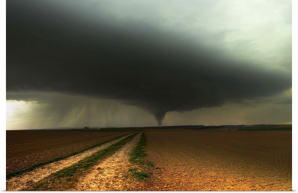 A tornado extends into the horizon from storm-clouds overhead, seen from across farmland.