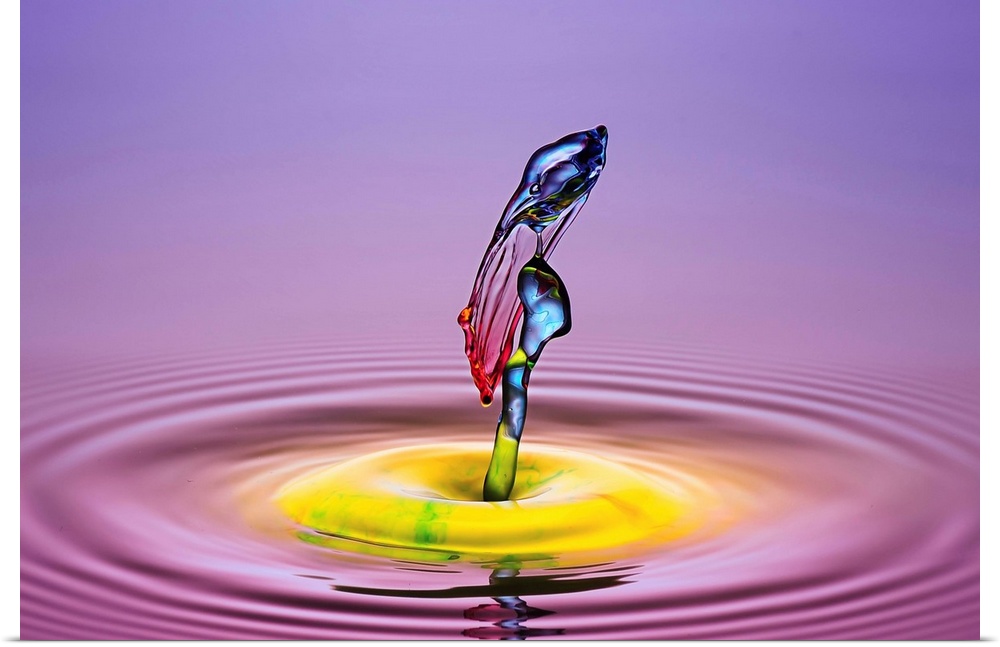 A macro photograph of a drop of water caught suspended in mid-air against a vibrant colorful background.