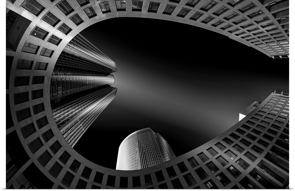Black and white architectural abstract photograph of a horseshoe building with other buildings shooting up beside it.