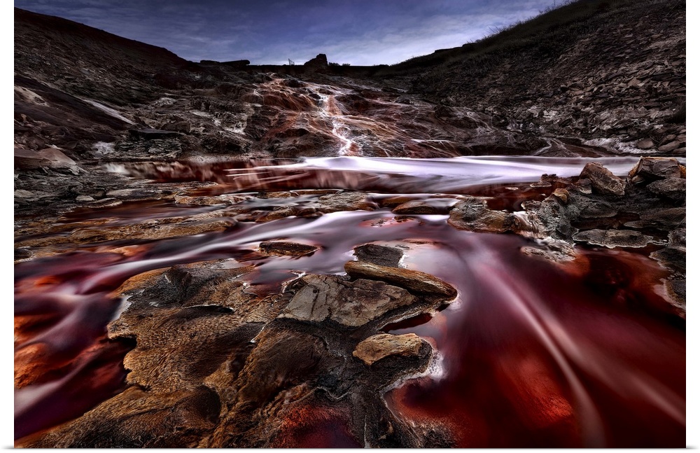 A red river flows through a rock landscape under a crescent moon, Spain.