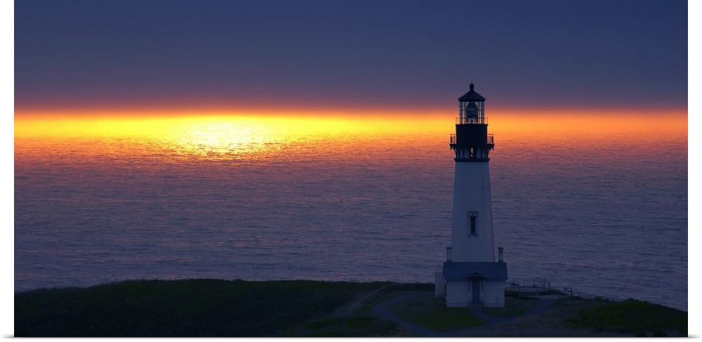 Landscape photograph of an unlit lighthouse at sunset by the ocean.