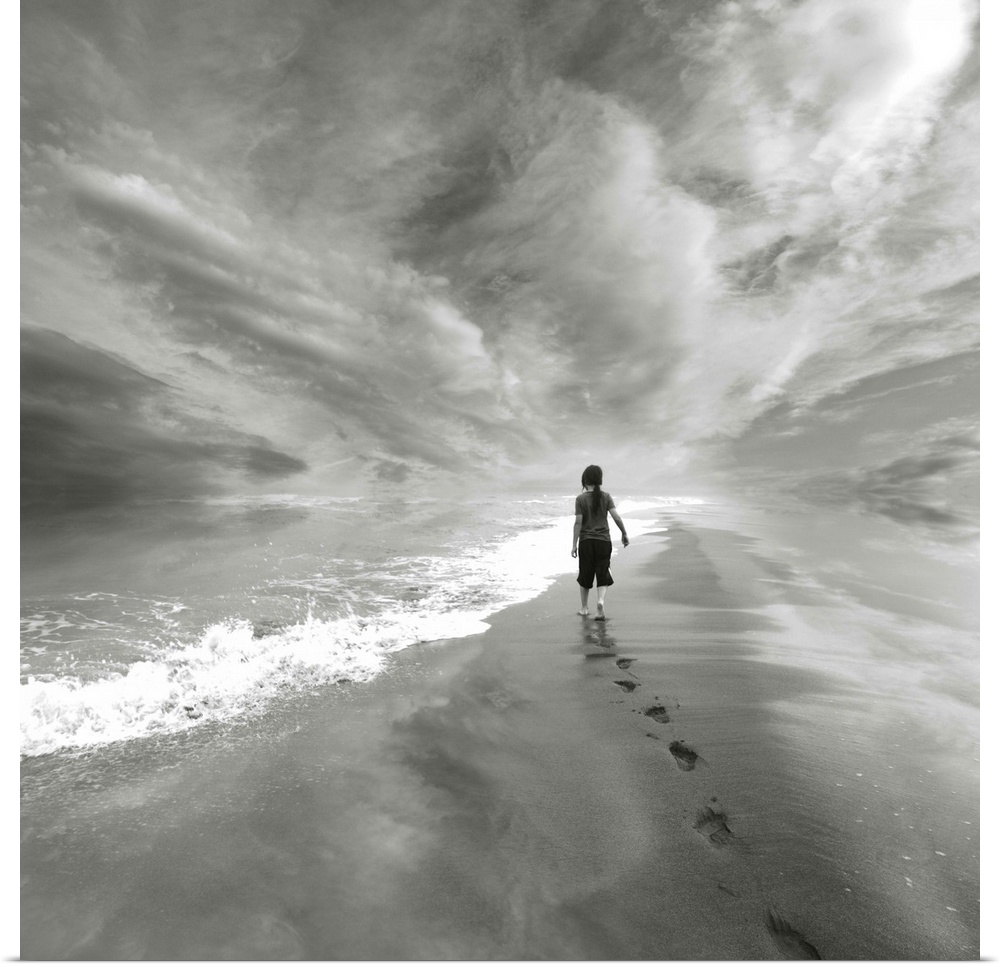 A young child walks along the beach to the edge of the water, leaving a trail of footprints behind.