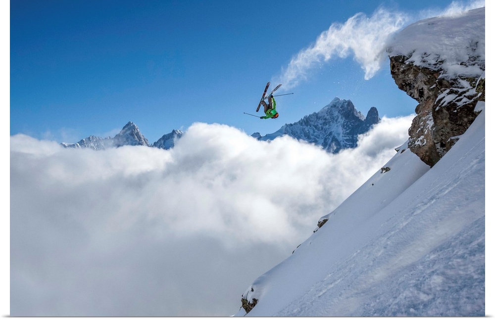 A skier leaps off a mountain in France, kicking off snow from the ends of the skies.