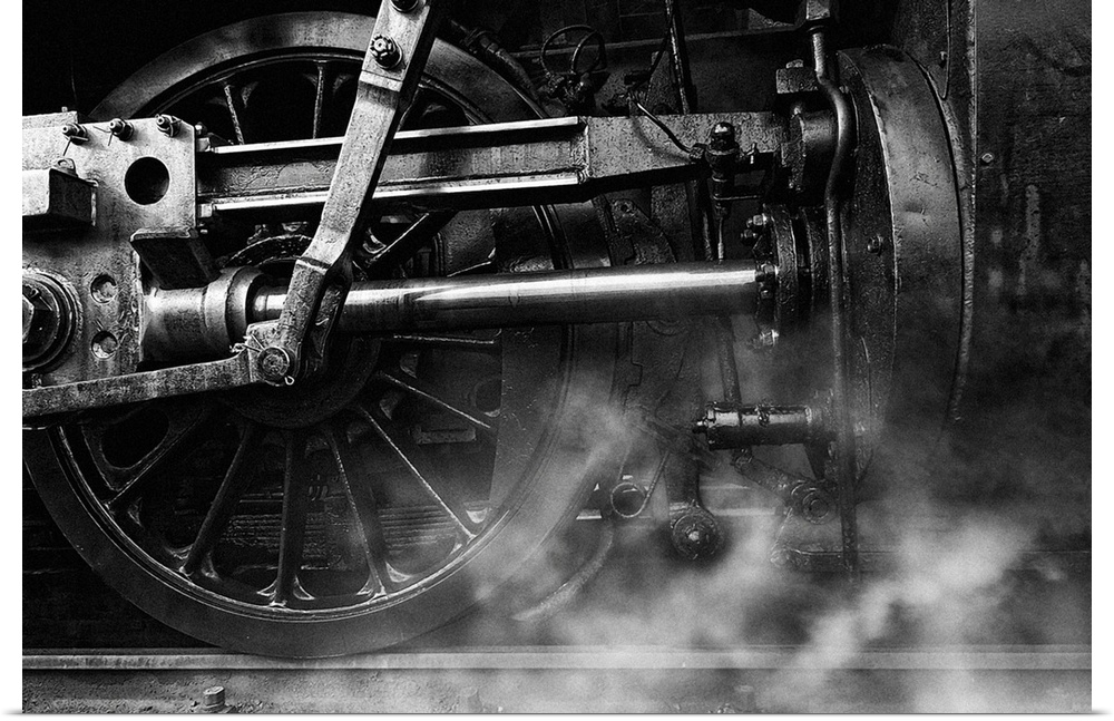 Steam rising from the pistons near the wheels of a train locomotive.