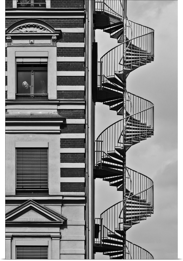 A spiral staircase against a building in Berlin, with a man looking out one of the windows.