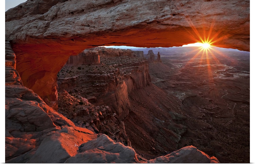 The sun framed by a large natural arch and the horizon, Canyonlands National Park, Utah.
