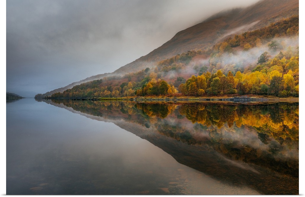 Landscape photograph of reflective Autumn mountains with light fog on a lake.