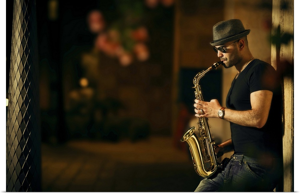 A man playing a saxophone in the street at night.