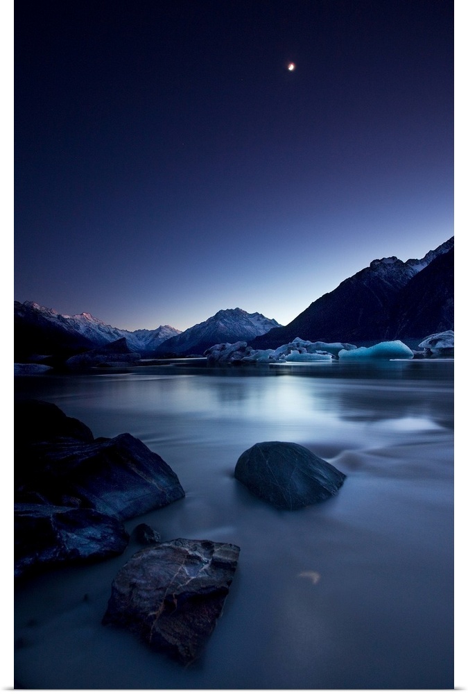 View of the moon over a river and snowy mountains in the evening, New Zealand.