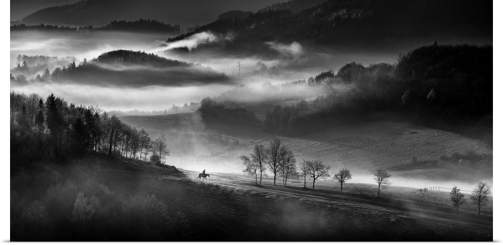 Black and white landscape with fog in the valley and a person riding a horse in the foreground.