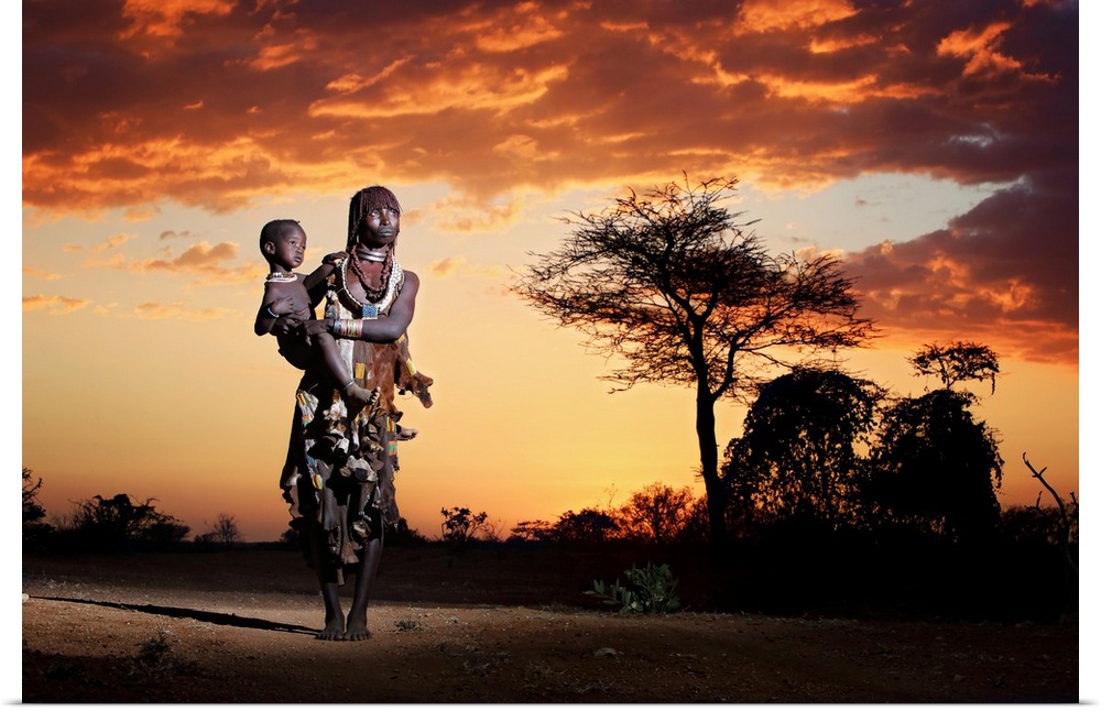A portrait of a tribes-woman holding her child underneath a sunset sky.