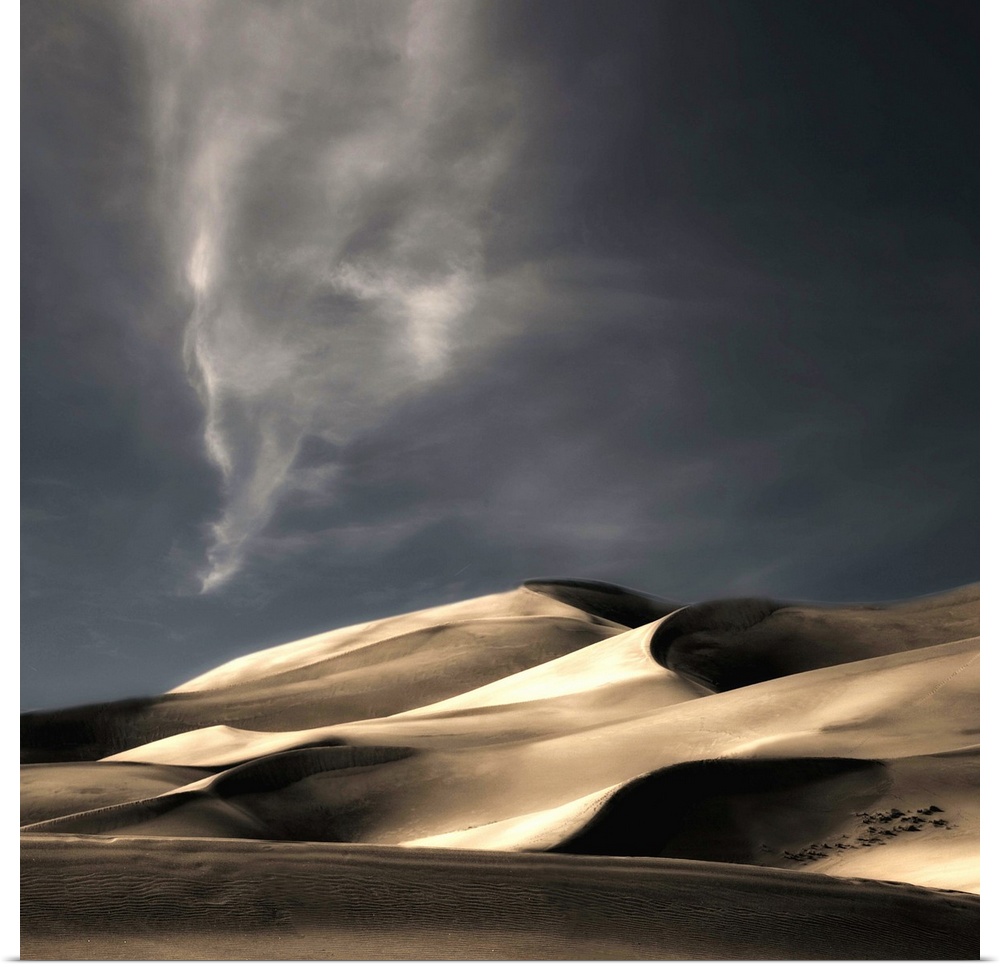 Desert sand dunes casting deep shadows under a darkening sky, Colorado.