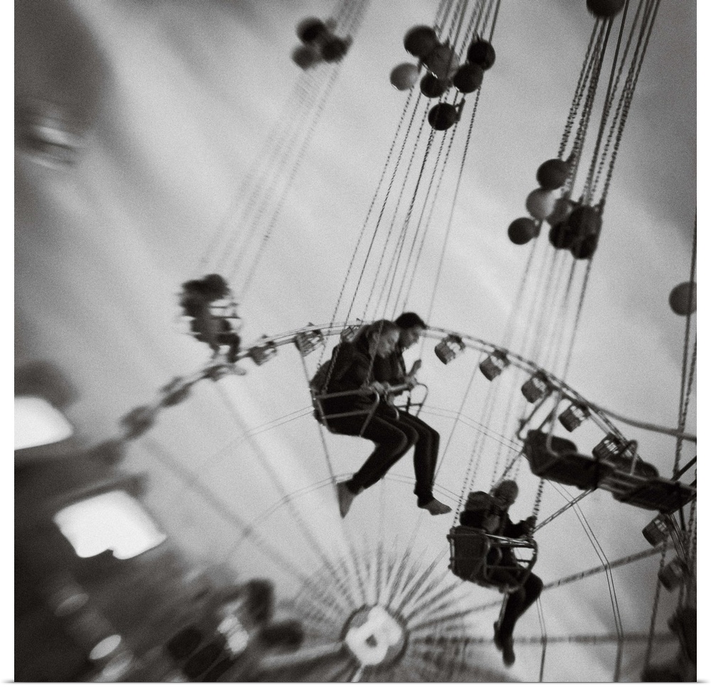 People swinging on an amusement park ride with a ferris wheel behind, Tivoli, Denmark.
