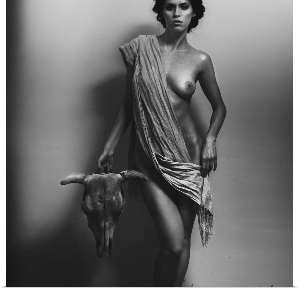 A black and white portrait of a nude woman draped in a cloth holding a bull skull.