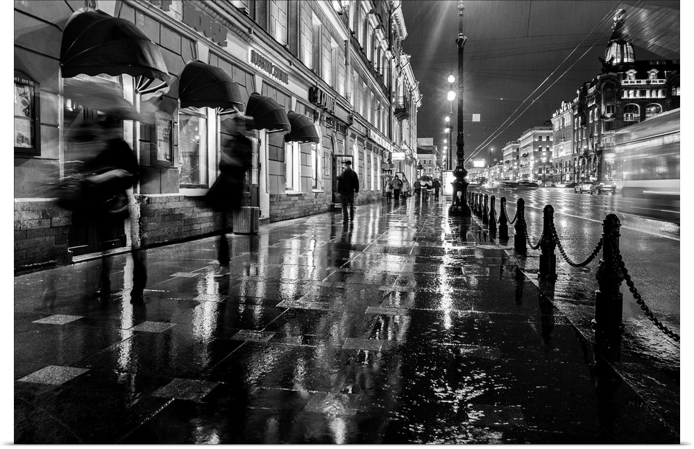 People walking on a sidewalk in the city at night, trying to get out of the rain.