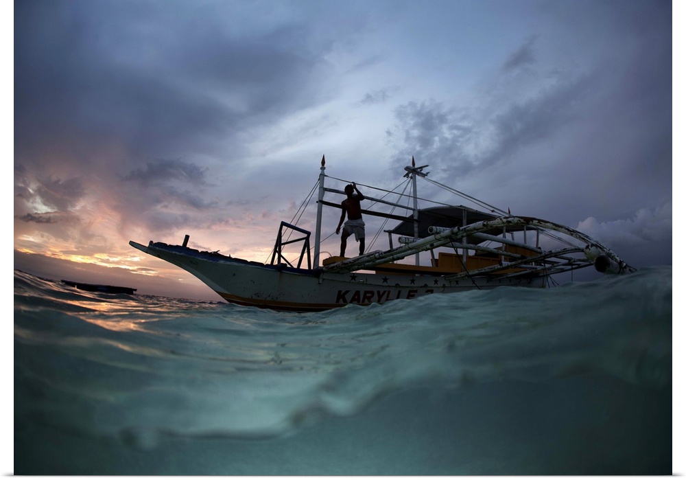 View from the surface of the water of a figure on a boat at sunset, Philippines.