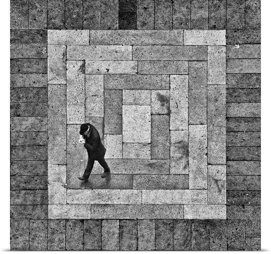 A man walking on a stone street which creates a square when viewed form above.