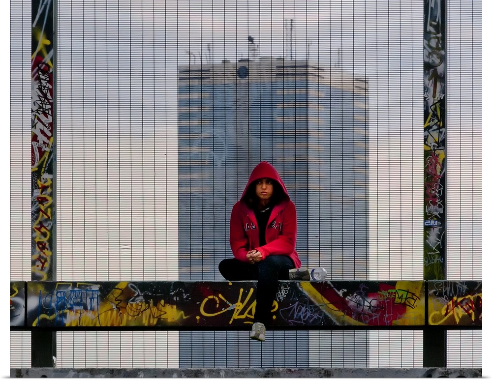 Person sitting on a graffiti-covered railing with a skyscraper directly behind them.
