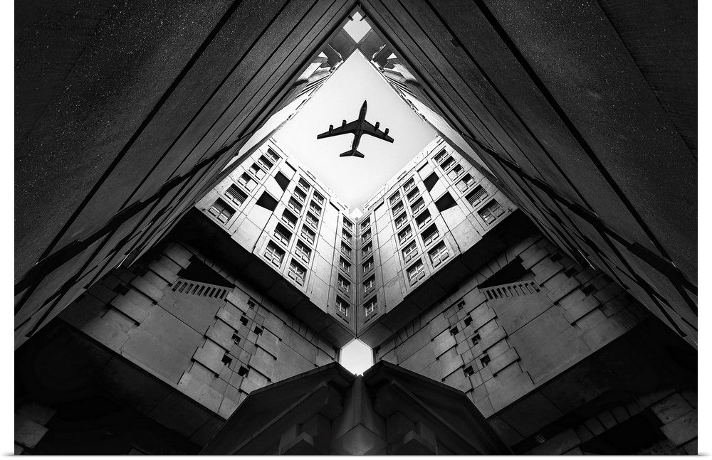Looking up through the courtyard of a building to see an airplane flying above.