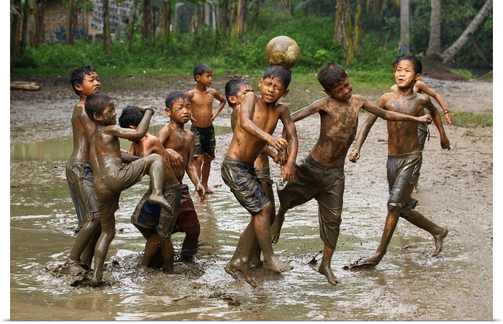 A group of young boys playing soccer in muddy water.