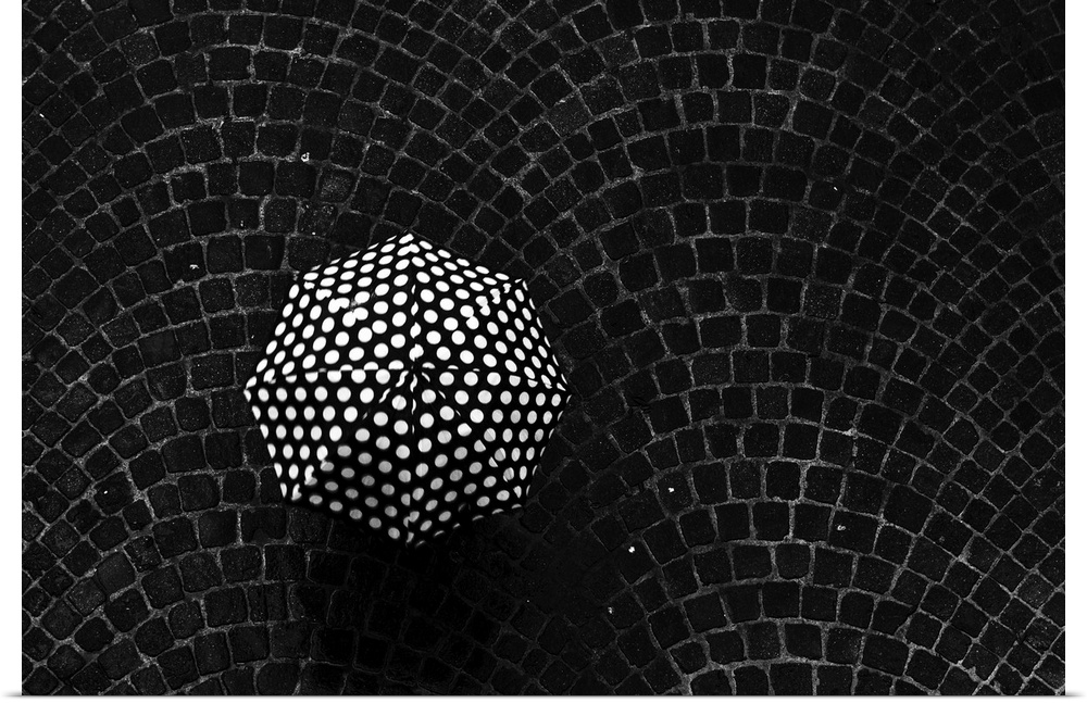 Aerial view of a polka dot umbrella held by someone standing on a cobblestone street.