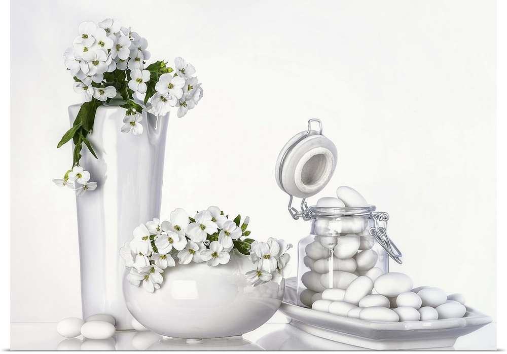Two white vases, tall and short, with white flowers, and a jar and dish of white jordan almonds.
