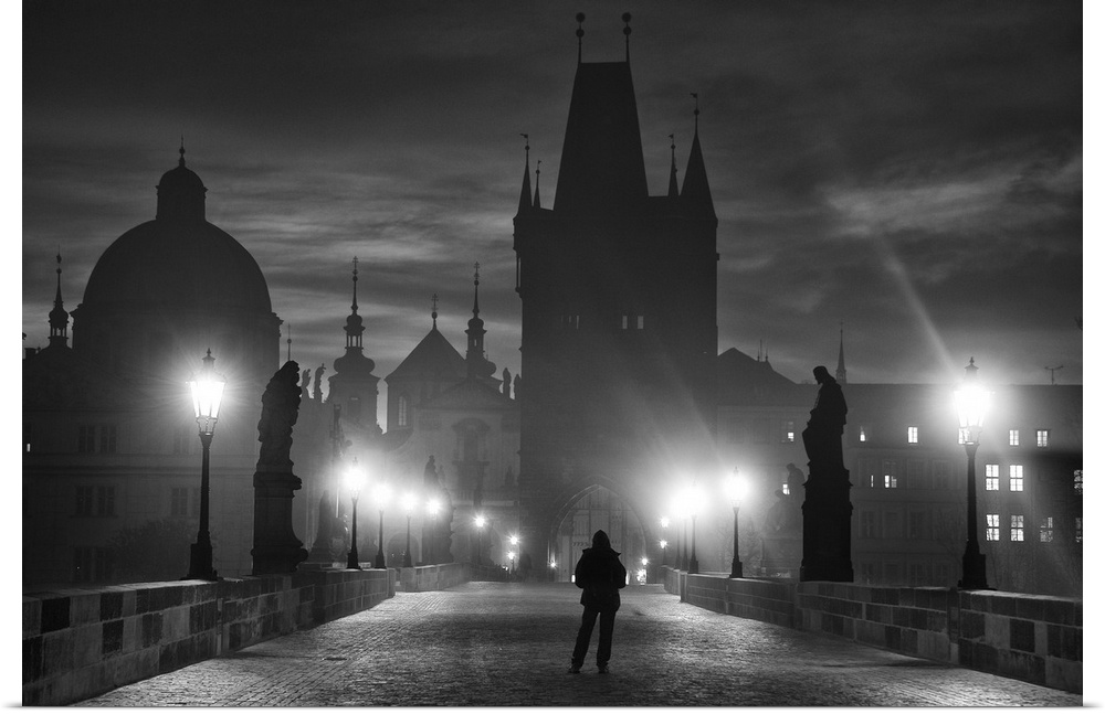 A silhouetted figure stands on a bridge at night facing the city of Prague, Czech Republic.