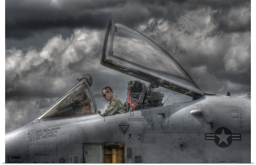 A US Air Force pilot sitting in the cockpit of his plane with dark clouds overhead.