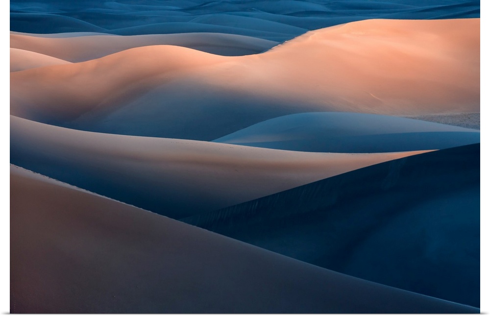A desert landscape with tall blue and orange sand dunes in the evening.