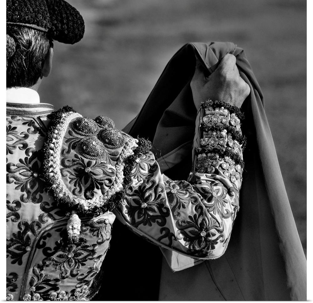 A matador in a beautifully detailed costume holds up a cape.