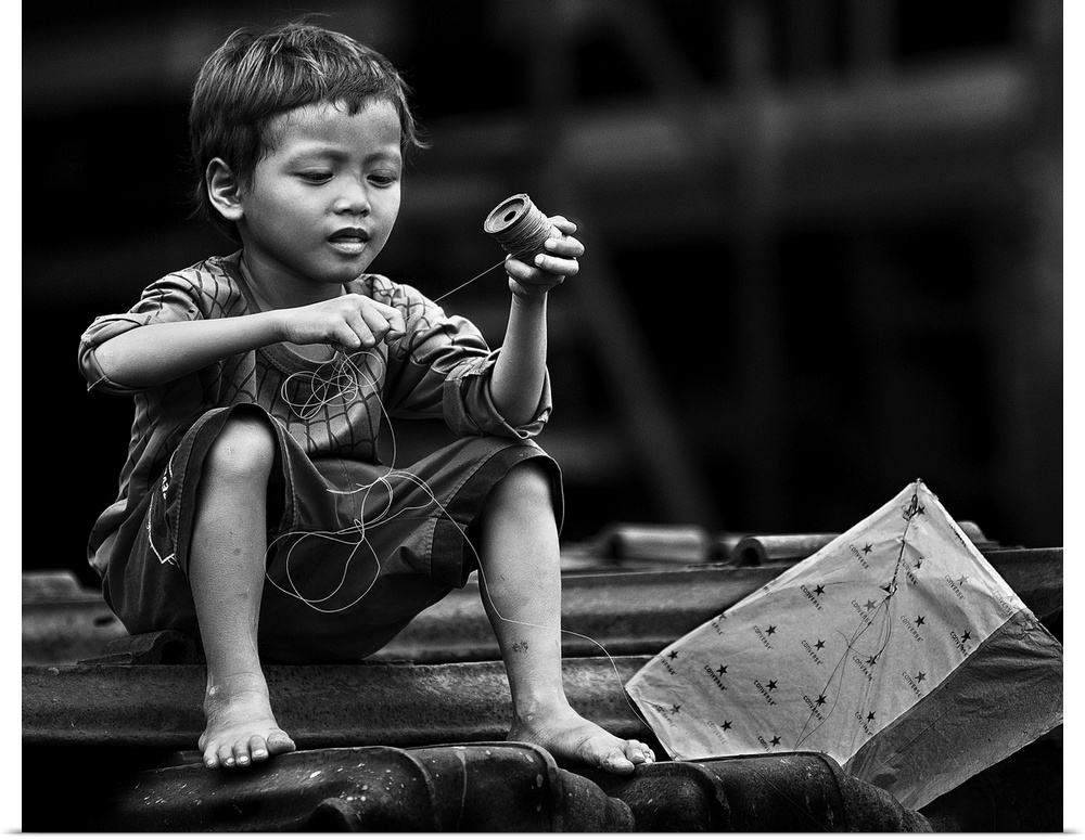 Black and white image of a boy winding the string of his kite.