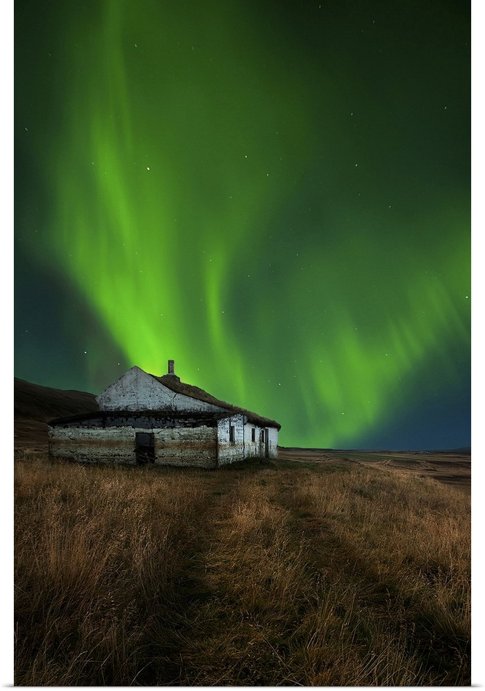An abandoned house in a field in Iceland, with a brilliant northern lights display in the skies above.