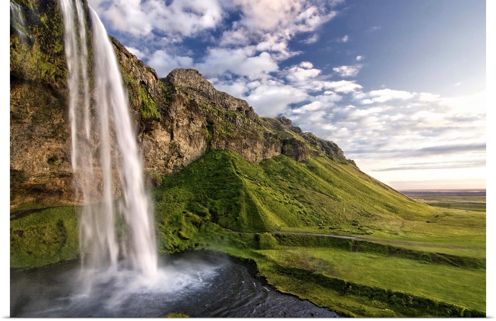 Waterfall on the side of a cliff in a lush valley in Iceland.