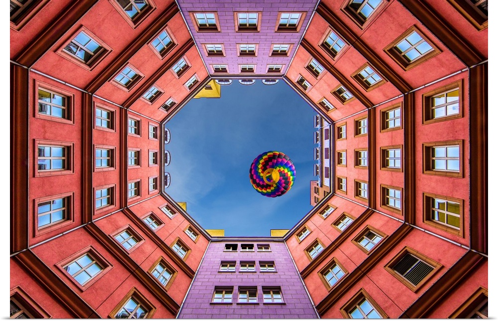 Photograph looking up from the middle of a courtyard at a colorful hot air balloon.