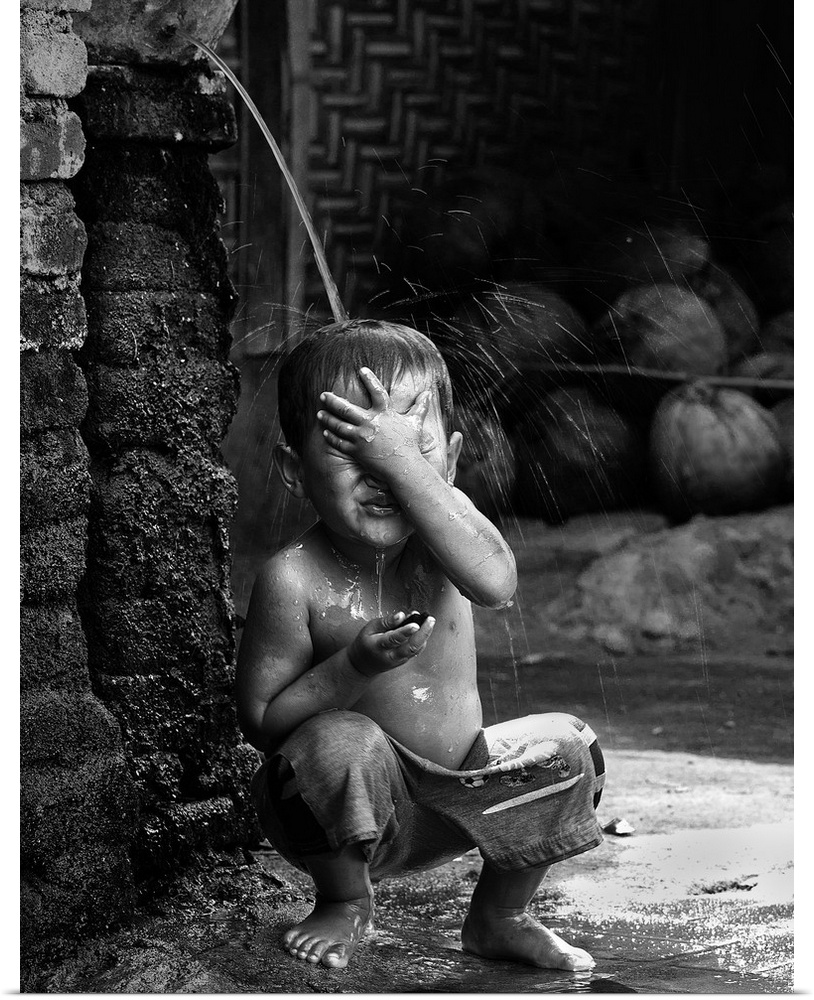 A young boy sits under a stream of water in the village of Sade, Lombok, Indonesia.