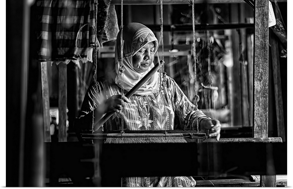 An old woman weaving away on a songket maker.