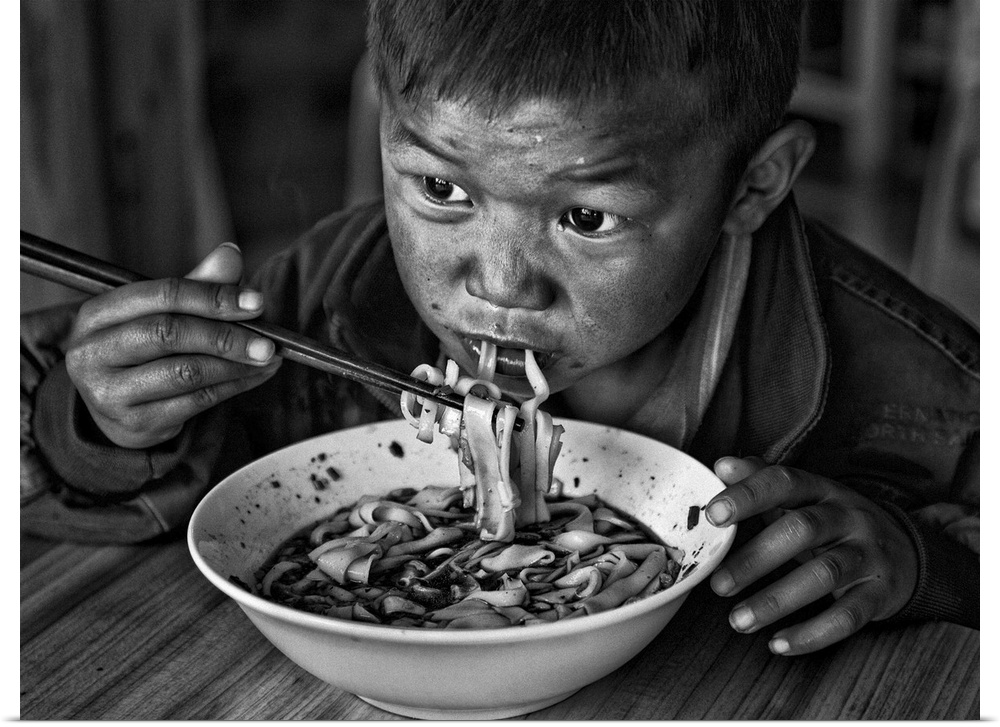 A young boy eats a bowl of noodles with chopsticks.
